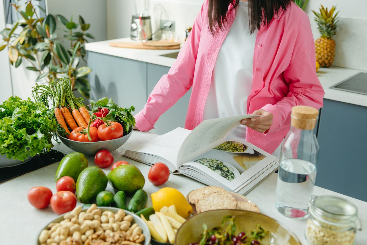 A person standing in a kitchen, surrounded by fresh fruits and vegetables, looking at a cookbook, symbolizing a focus on diet, lifestyle, and health. The background shows other various healthy food options, emphasizing the connection between diet, epigenetics, and overall well-being.